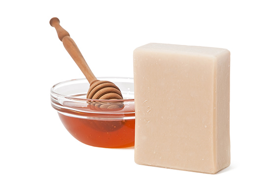 Milk-Honey soap bar and honey in a glass bowl with wooden dipper on the side.