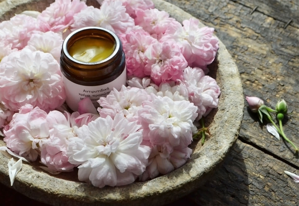 Anti-wrinkle face cream jar open and set around fluffy pink roses on a gray carved stone plate, on a rustic wooden surface