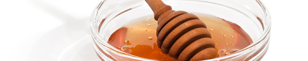 Honey in a glass bowl with wooden dipper (closeup)
